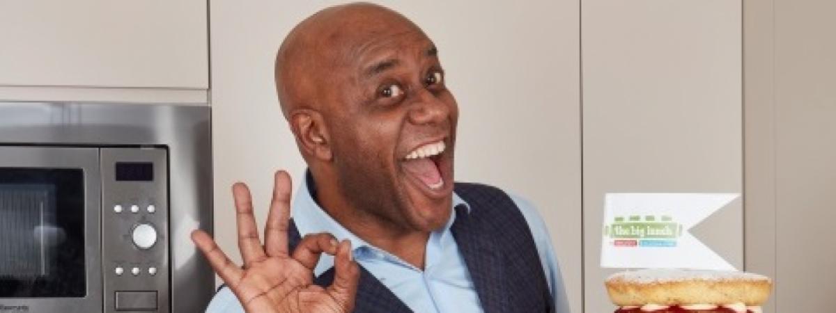 ainsley harriot with big lunch flag and cake looking delighted and holding fingers up to make ok sign