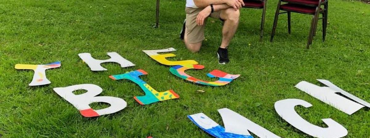 the big lujnch letters on teh grass with a man preparing to invite a few neighbours over for a chat as part of the big Lunch month of community