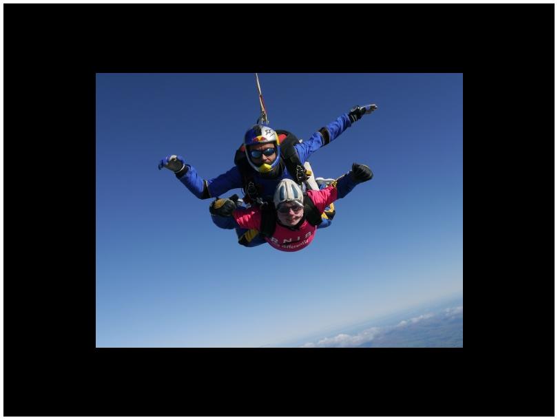 tandem skydivers falling through the blue sky, one wearing a pink RNIB tshirt