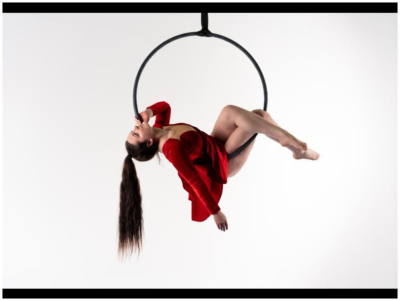 A black trapese hoop holding a girl wearing short glamorous dress and swinging a long brown ponytail hairstyle