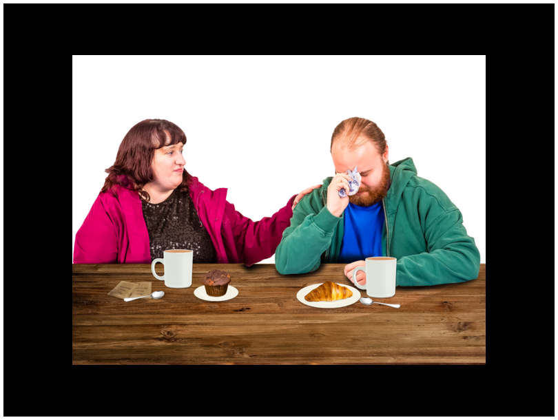A woman and a man are sitting at a table. The woman is consoling the man, who is visibly upset.