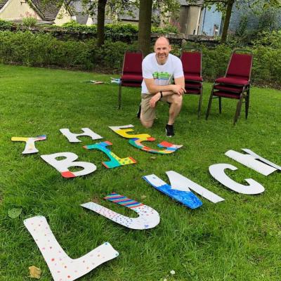 the big lujnch letters on teh grass with a man preparing to invite a few neighbours over for a chat as part of the big Lunch month of community
