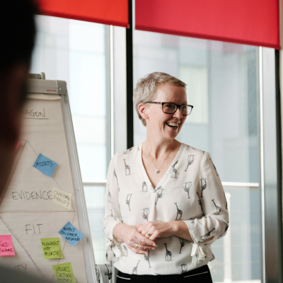 White woman in white blouse standing by a flip chart with a smile on her face